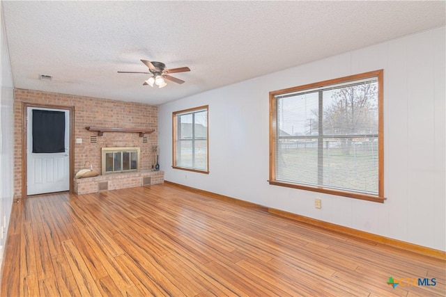 unfurnished living room with baseboards, ceiling fan, a textured ceiling, light wood-type flooring, and a fireplace