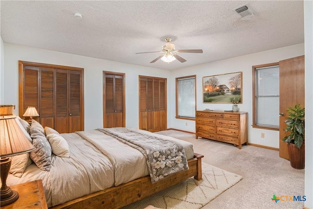 bedroom featuring a textured ceiling, light colored carpet, visible vents, baseboards, and two closets