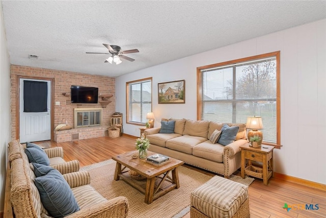 living room with visible vents, light wood-style floors, ceiling fan, a textured ceiling, and a brick fireplace