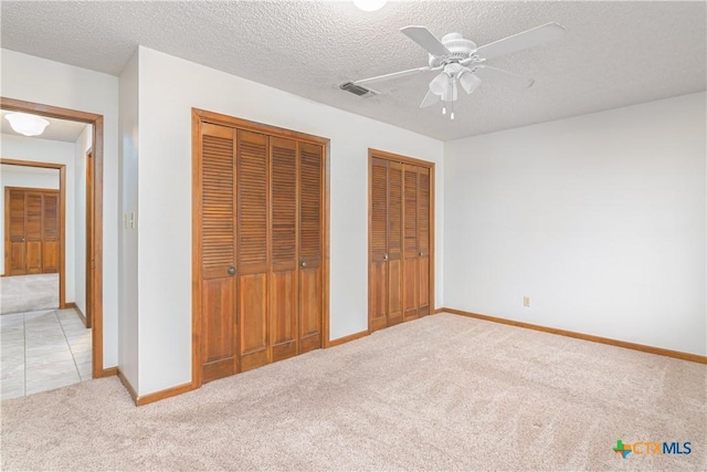 unfurnished bedroom with light carpet, a textured ceiling, visible vents, and two closets