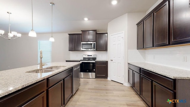 kitchen with sink, hanging light fixtures, stainless steel appliances, dark brown cabinetry, and light stone countertops