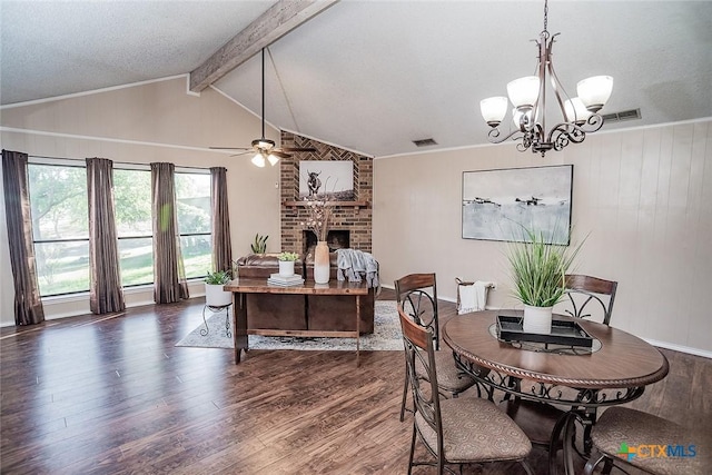 dining space featuring visible vents, a fireplace, wood finished floors, ceiling fan with notable chandelier, and vaulted ceiling with beams