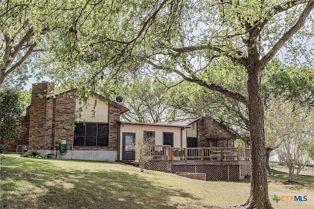 back of house with a wooden deck, brick siding, a yard, and a chimney