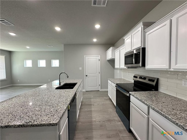 kitchen featuring dishwasher, electric stove, an island with sink, white cabinetry, and sink