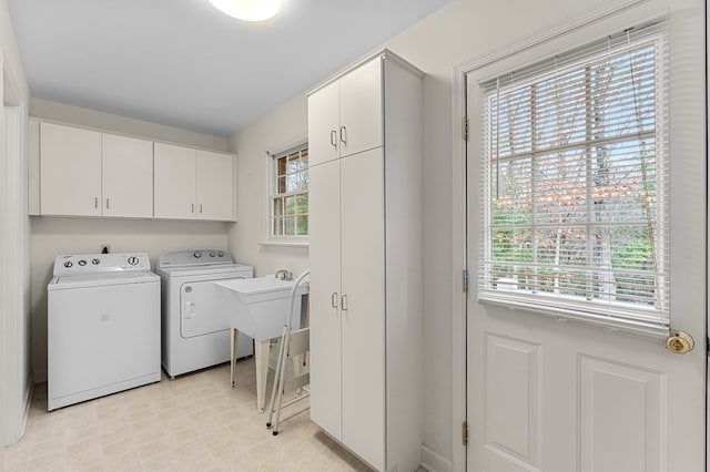 laundry room featuring washer and clothes dryer, a healthy amount of sunlight, and cabinets