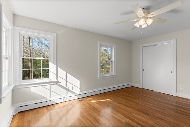 spare room with a healthy amount of sunlight, ceiling fan, a baseboard heating unit, and hardwood / wood-style floors