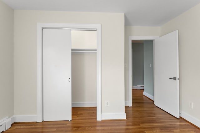 unfurnished bedroom with dark hardwood / wood-style floors and a baseboard heating unit