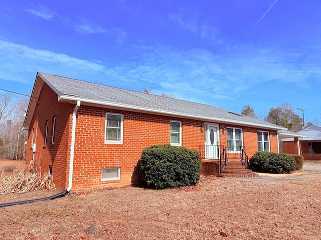 ranch-style house featuring brick siding and roof with shingles