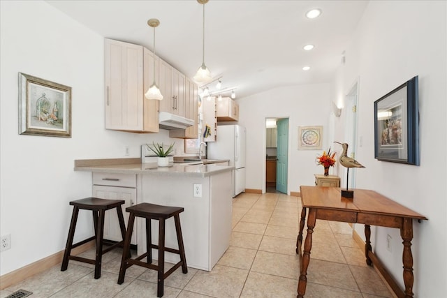 kitchen featuring under cabinet range hood, a kitchen breakfast bar, freestanding refrigerator, a peninsula, and light countertops