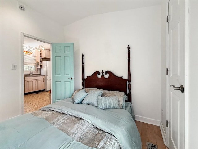 bedroom with visible vents, lofted ceiling, light wood-style flooring, freestanding refrigerator, and a sink