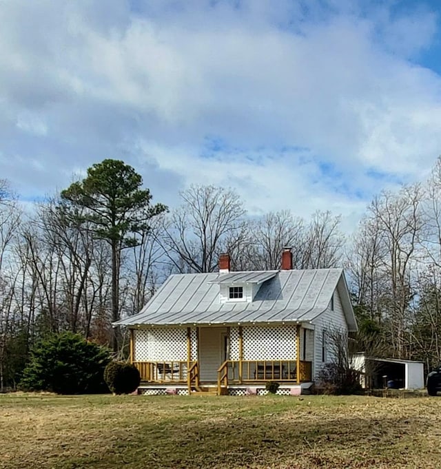 view of front of property with a standing seam roof, metal roof, a chimney, and a front lawn