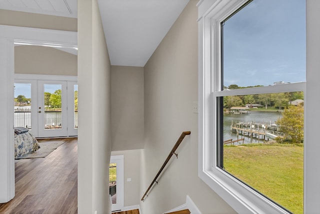 staircase with french doors, a water view, and wood finished floors