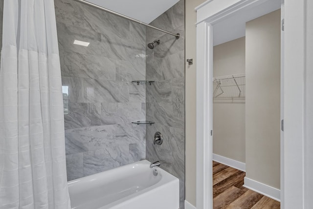 full bathroom with baseboards, a walk in closet, wood finished floors, and shower / tub combo