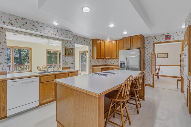 kitchen with a center island, white appliances, a kitchen breakfast bar, sink, and light wood-type flooring