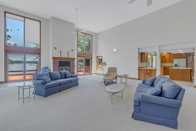 living room featuring ceiling fan, a water view, a high ceiling, and a brick fireplace