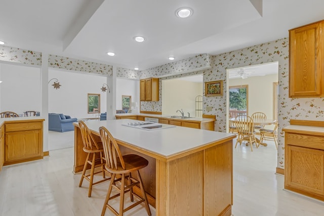 kitchen featuring ceiling fan, a center island, sink, kitchen peninsula, and a breakfast bar area