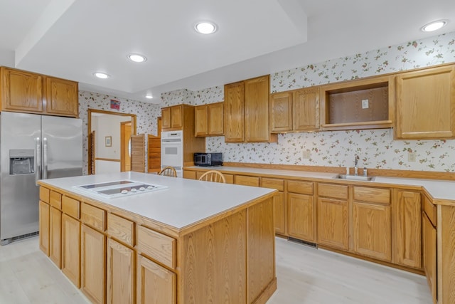 kitchen with sink, a kitchen island, white appliances, and light hardwood / wood-style flooring