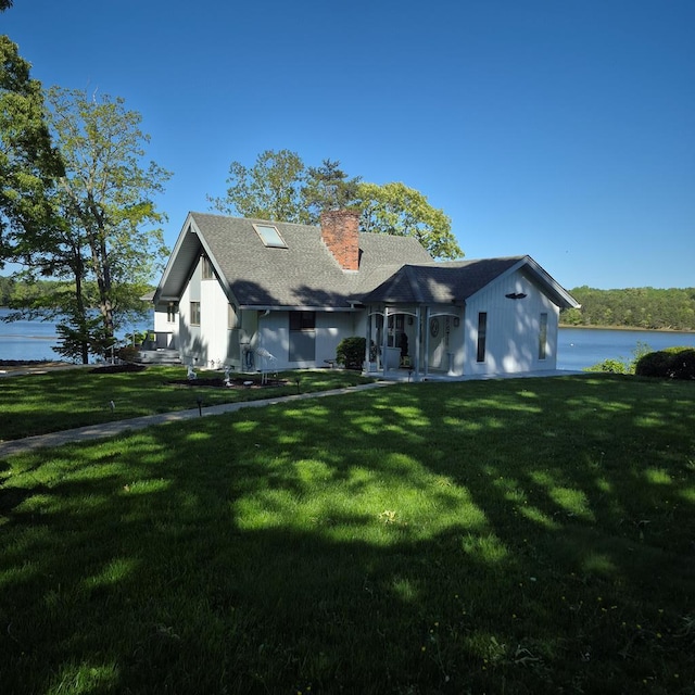 view of front of home with a chimney, a shingled roof, a front yard, and a water view