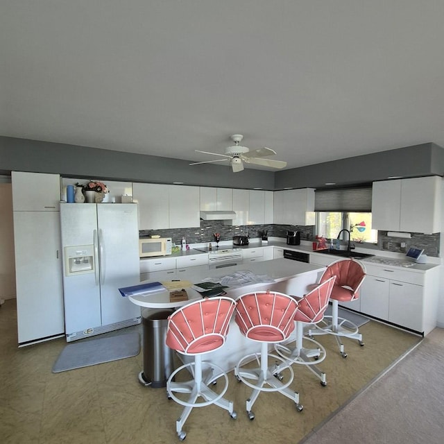 kitchen featuring tasteful backsplash, white appliances, white cabinets, and a center island