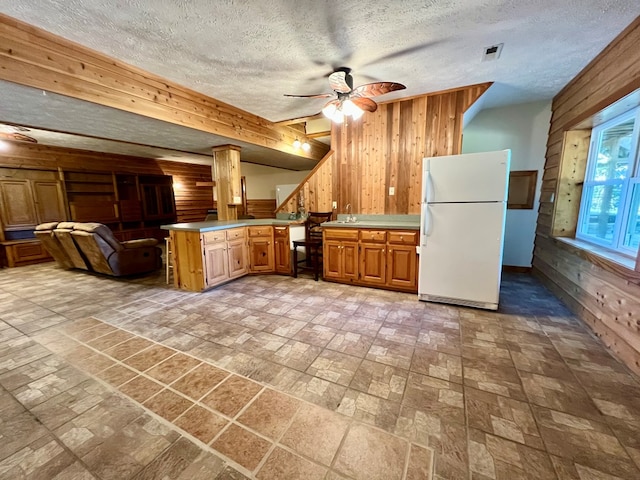 kitchen featuring kitchen peninsula, a textured ceiling, ceiling fan, white refrigerator, and wood walls