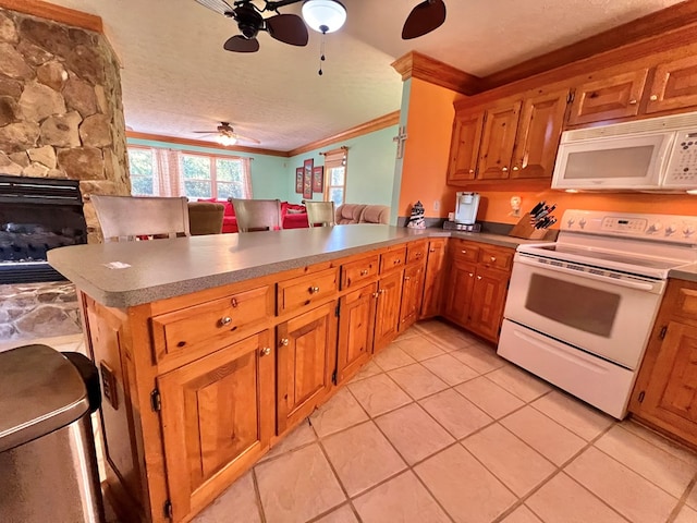 kitchen featuring kitchen peninsula, white appliances, crown molding, light tile patterned floors, and a stone fireplace