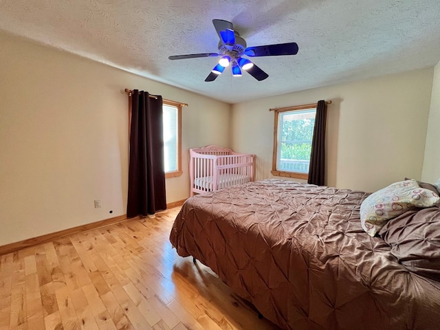 bedroom with multiple windows, ceiling fan, a textured ceiling, and light wood-type flooring