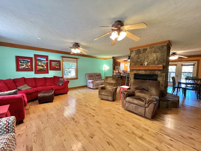 living room with ceiling fan, a stone fireplace, light wood-type flooring, a textured ceiling, and ornamental molding