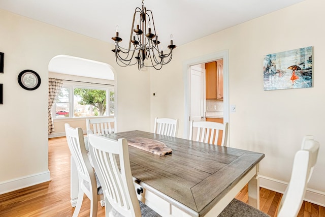 dining space featuring light wood-style floors, arched walkways, baseboards, and an inviting chandelier