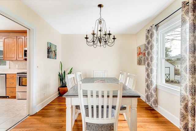 dining area with light wood-style floors, a notable chandelier, and baseboards