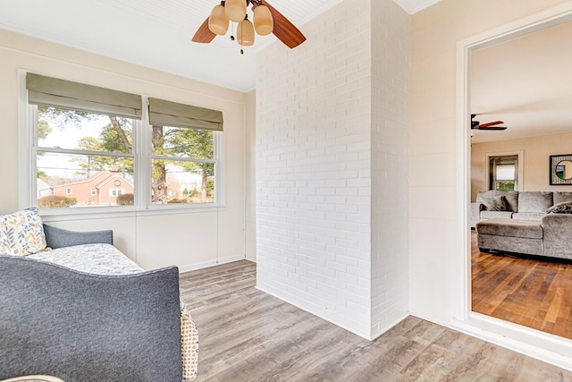 interior space with brick wall, ceiling fan, and wood finished floors