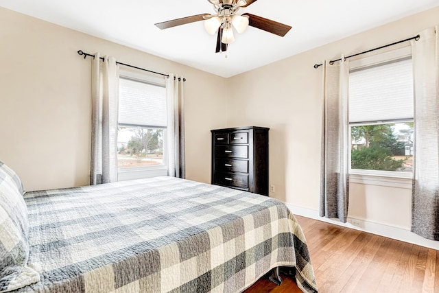 bedroom with multiple windows, wood finished floors, a ceiling fan, and baseboards