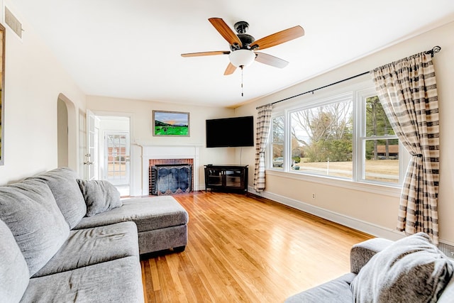 living room featuring arched walkways, visible vents, a brick fireplace, wood finished floors, and baseboards