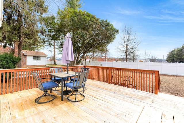 deck with a fenced backyard, outdoor dining area, and an outbuilding