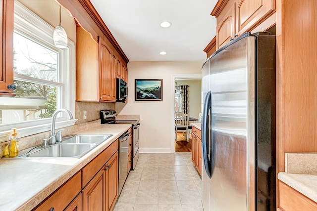 kitchen with light tile patterned floors, light countertops, hanging light fixtures, appliances with stainless steel finishes, and a sink