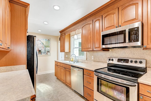 kitchen with stainless steel appliances, a sink, baseboards, light countertops, and backsplash