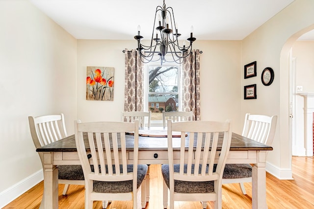 dining space with arched walkways, light wood-style flooring, baseboards, and an inviting chandelier