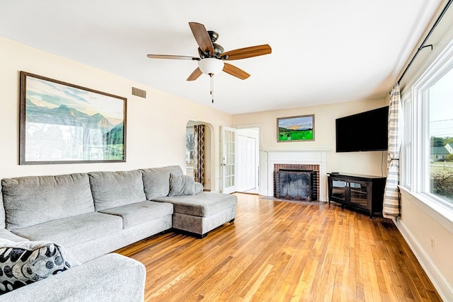 living area featuring baseboards, visible vents, arched walkways, light wood-type flooring, and a brick fireplace