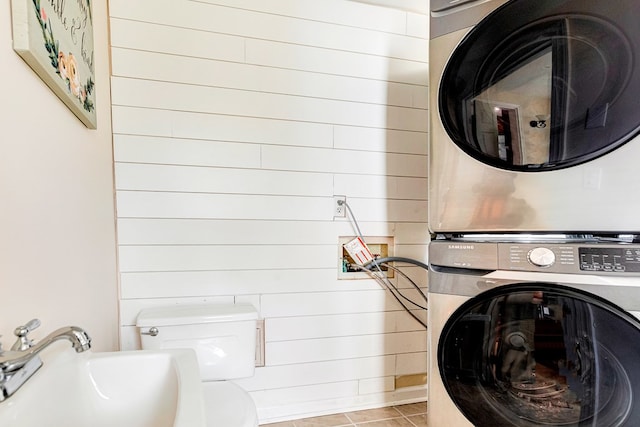 washroom featuring light tile patterned floors, laundry area, wood walls, a sink, and stacked washer / drying machine