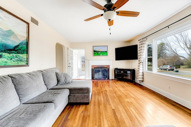 living room featuring arched walkways, a fireplace, wood finished floors, visible vents, and baseboards