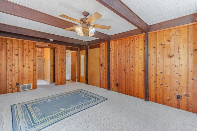 unfurnished room with carpet floors, ceiling fan, wooden walls, and beamed ceiling