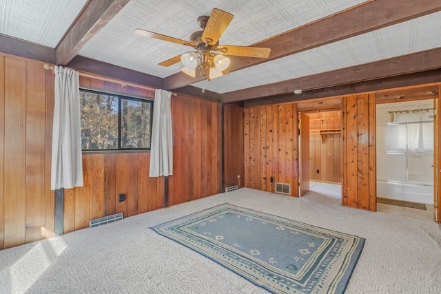 empty room featuring carpet flooring, ceiling fan, wooden walls, and beamed ceiling