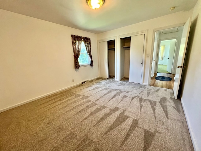 unfurnished bedroom featuring light carpet and two closets