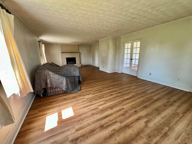 unfurnished living room featuring french doors, a textured ceiling, light hardwood / wood-style flooring, and a brick fireplace