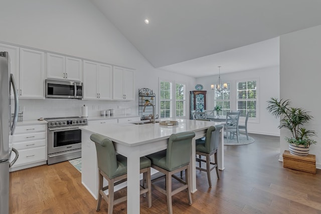 kitchen with pendant lighting, a breakfast bar area, stainless steel appliances, light hardwood / wood-style floors, and white cabinets