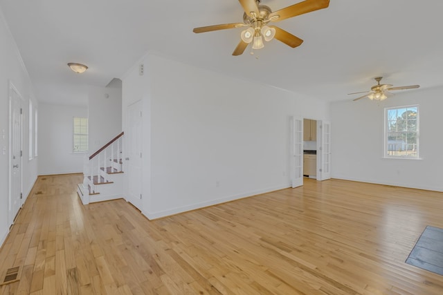 unfurnished living room with plenty of natural light, stairway, light wood-type flooring, and visible vents