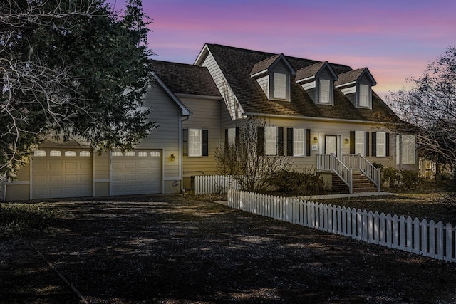 cape cod house featuring a fenced front yard, driveway, and a garage