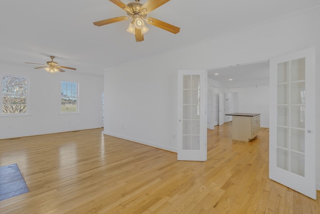 empty room featuring french doors, light wood-type flooring, a ceiling fan, and baseboards