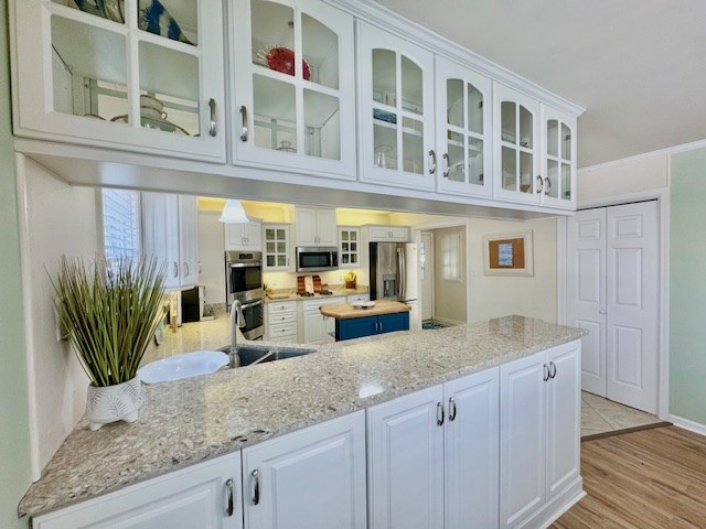 kitchen with glass insert cabinets, appliances with stainless steel finishes, light wood-style floors, white cabinetry, and a sink