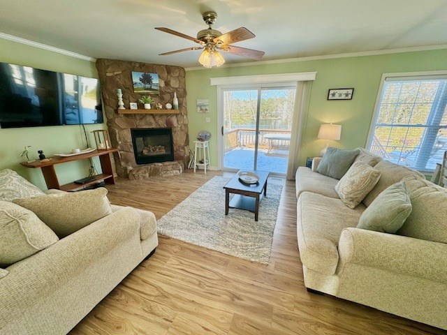 living area featuring a ceiling fan, a stone fireplace, crown molding, and wood finished floors