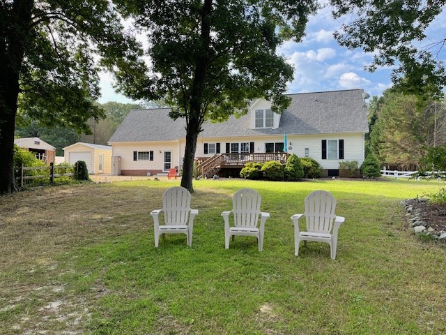 back of property featuring a garage, fence, a deck, and a lawn